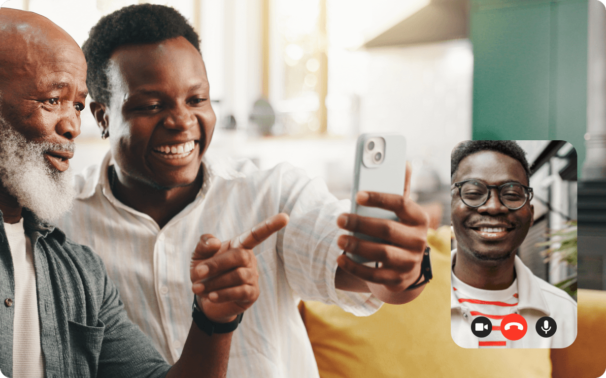 Two smiling men sit together on a couch, taking a selfie during a video call with a third smiling man shown in a small on-screen window, perhaps discussing Ethiopia remittances. The atmosphere is bright and cheerful.