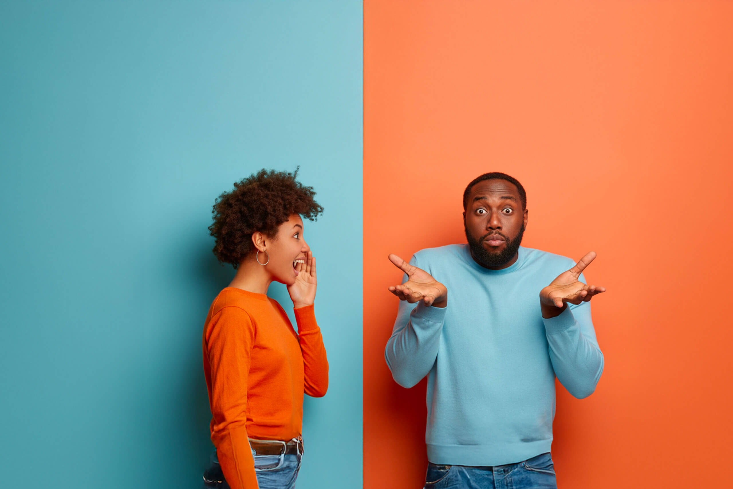 A woman in an orange sweater whispers with surprise to a man in a light blue sweater who stands next to her, shrugging with a puzzled expression. The background is split blue and orange.
